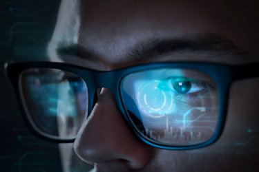 A SOC analyst's glasses reflecting data displayed on a a computer screen